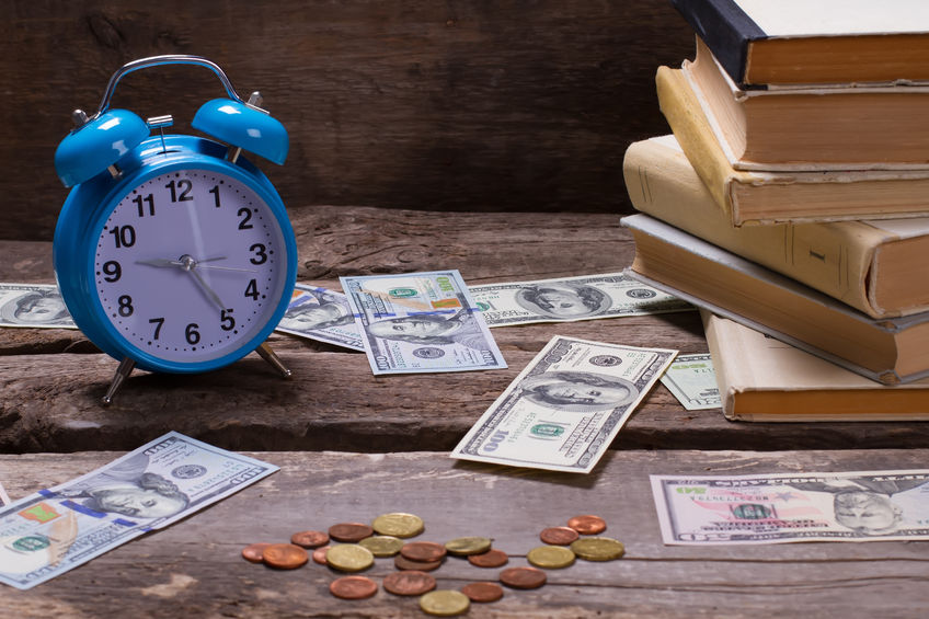 old books, alarm clock and money on a vintage wooden background.