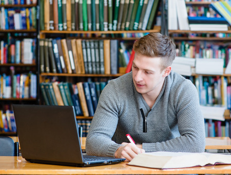 male student with laptop studying in the university library