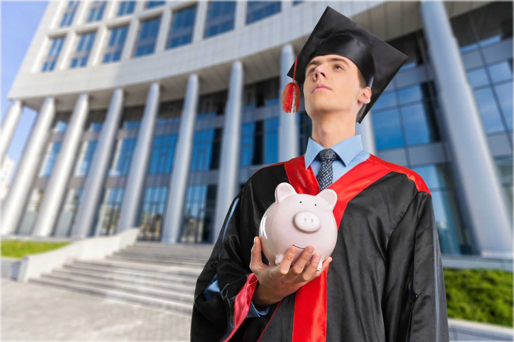 male student in graduation cap and gown holding piggy bank concept for Kiwanis Scholarship