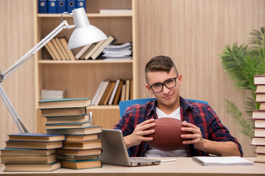young student studying holding a football concept for athletic scholarships vs academic scholarships
