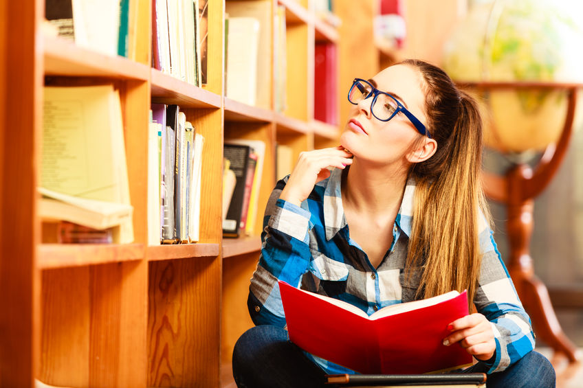top 10 study habits concept. clever female student hair ponytail girl blue glasses sitting on floor in college library with stack books. indoor