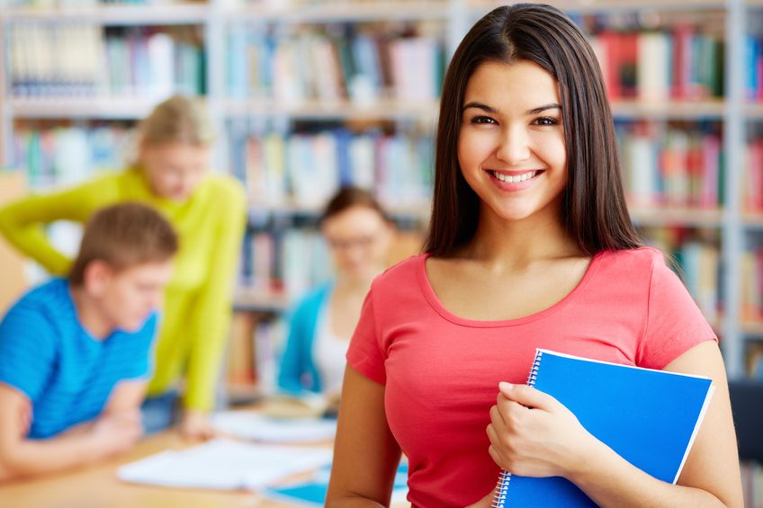 portrait of pretty girl looking at camera in college library with her group mates on background concept for Scholarships for continuing college students
