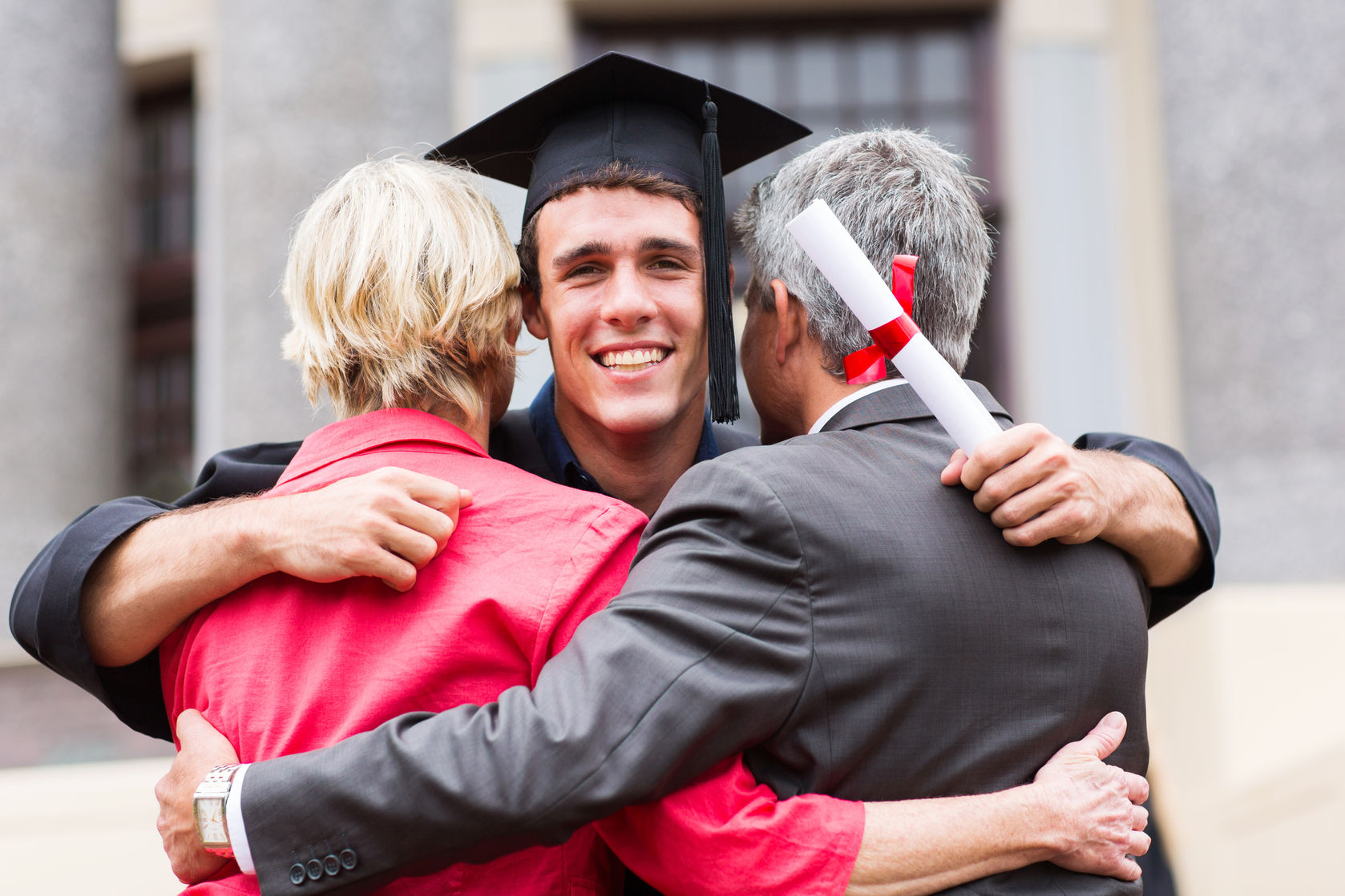 handsome young male graduate hugging his parents at graduation