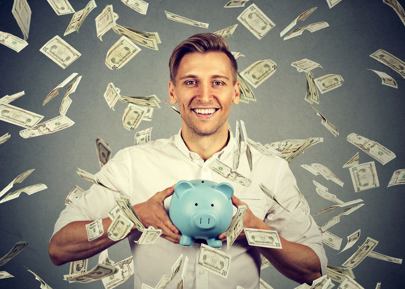 happy man with piggy bank celebrates success under money rain falling down dollar bills banknotes isolated on gray wall background. financial success concept for bank scholarships