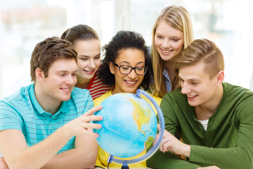 education, travel and geography concept - five smiling student looking at earth globe at school concept for How to Apply for a Scholarship to Study Abroad