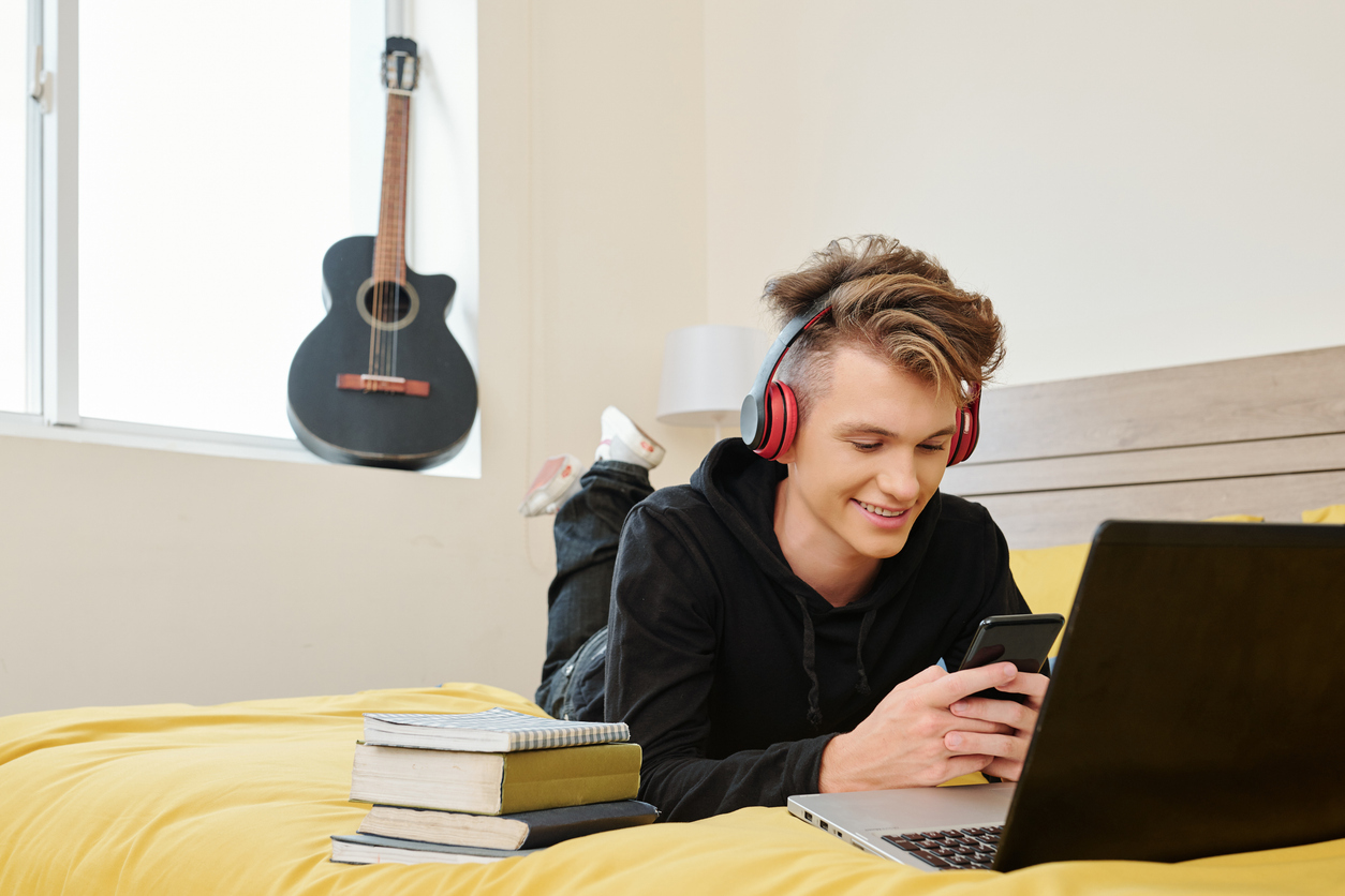 Student lying on bed with smartphone while exploring his natural talents for his college major