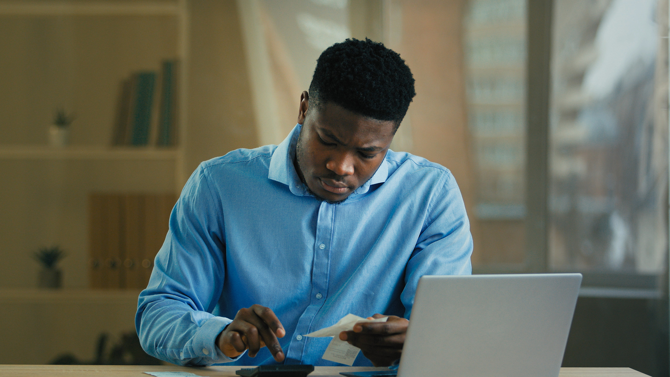 Young African american businessman man employee male count incomes bills manage personal budget use calculator calculate business expenses credit debt money balance managing finances financial economy