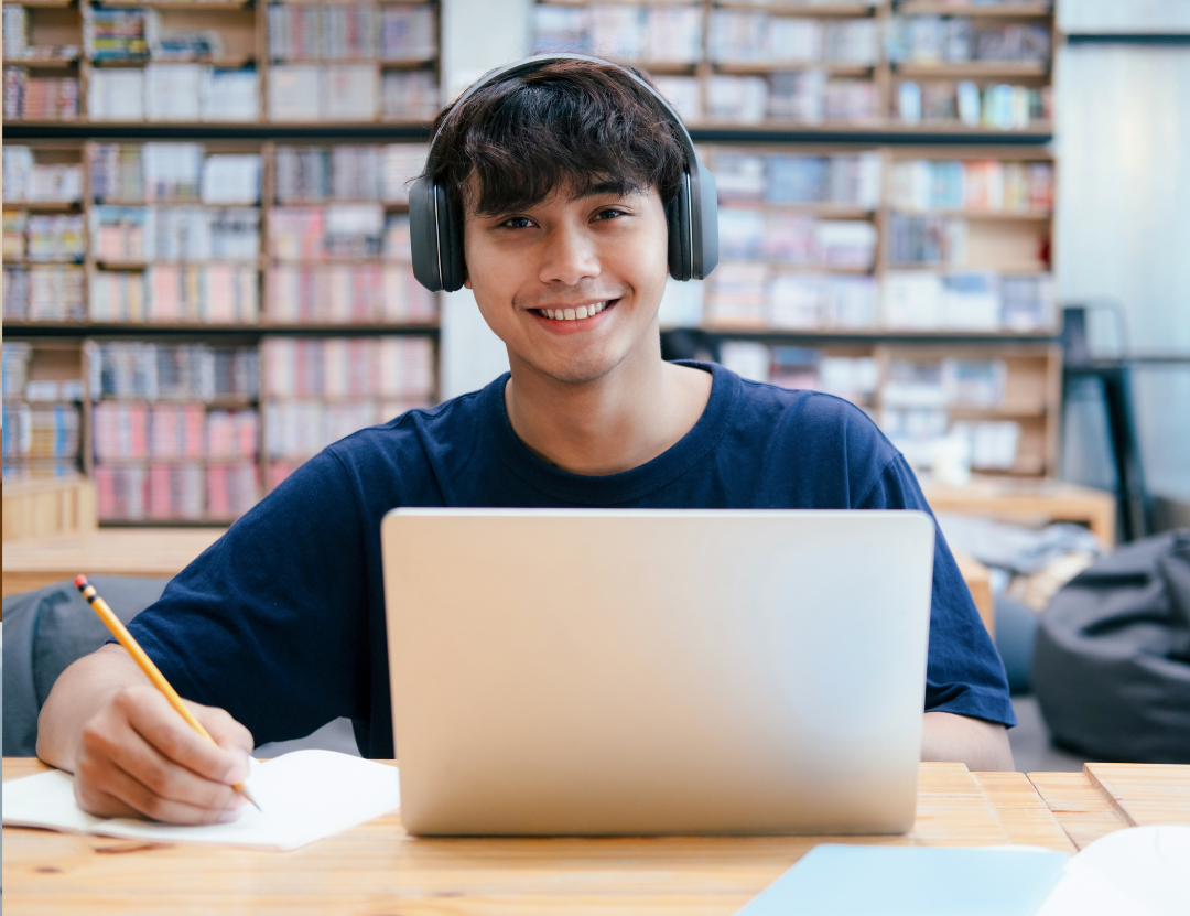 Student working on laptop smiling at camera showing scholarship success