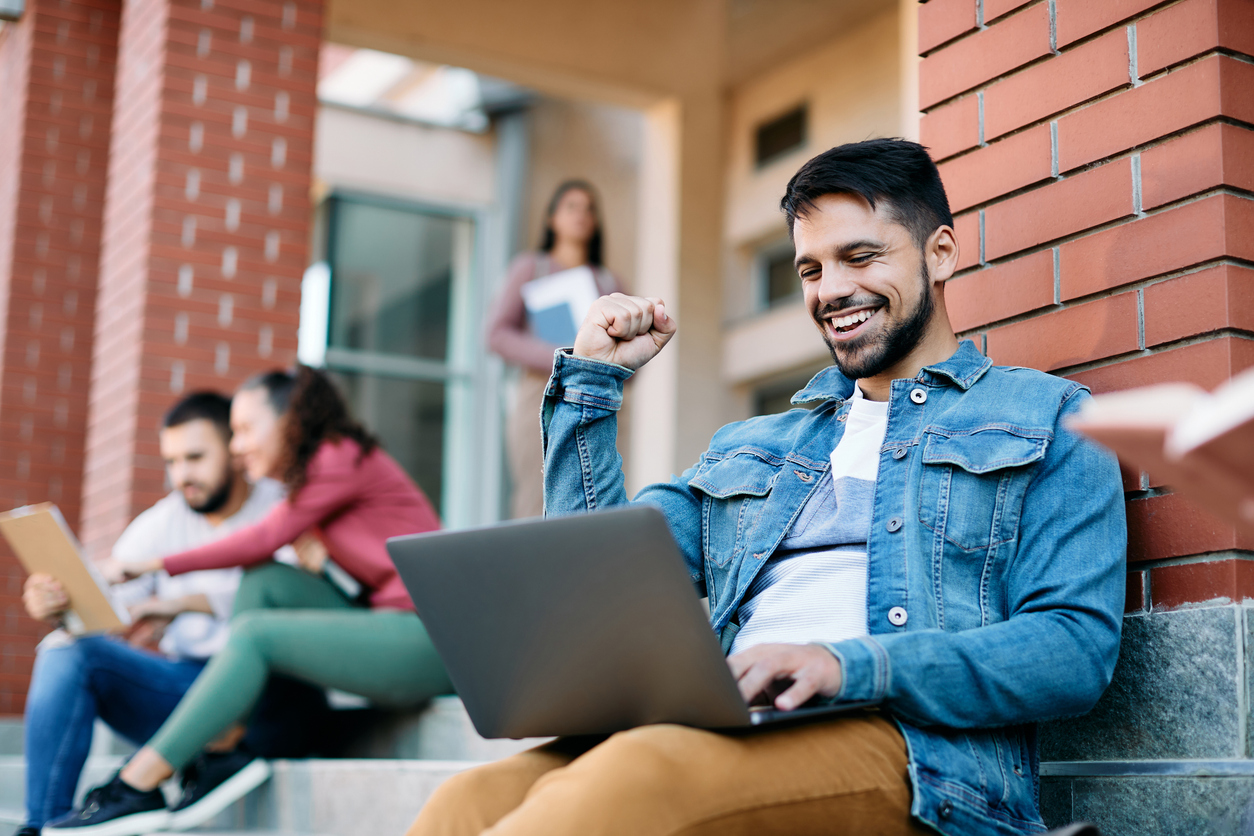 Happy student celebrating good news while using laptop at campus,