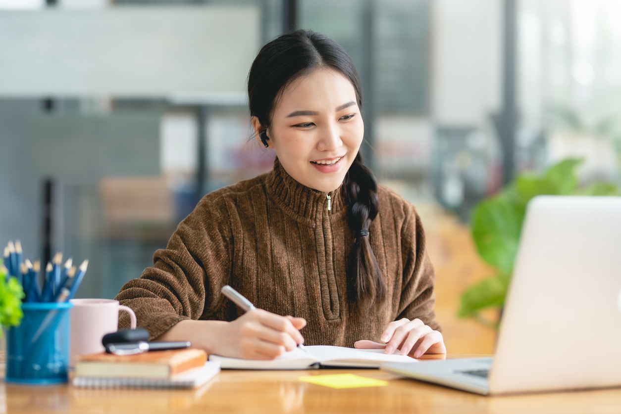 Pretty young Asian female student studying online on laptop computer.