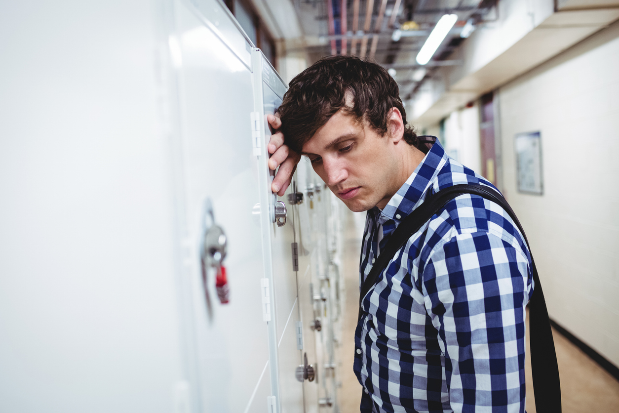 Sad student leaning on locker